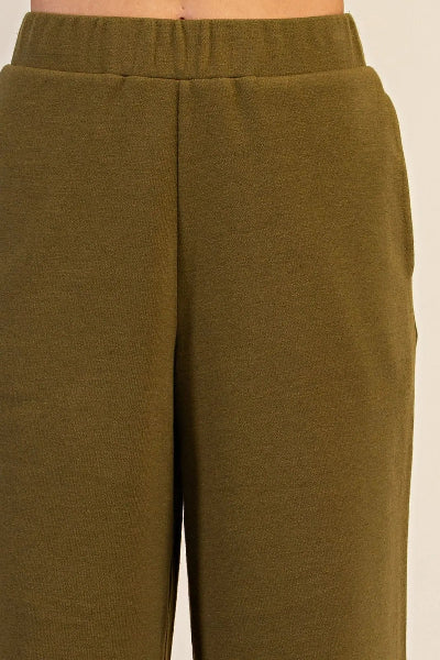 Close-up of olive green wide-leg sweatpants worn by a model, showing the textured fabric, side pocket seam, and elastic waistband.