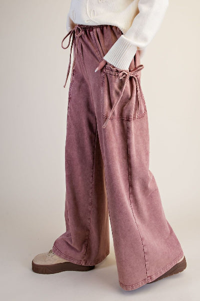 A person wearing wide-leg dusty rose corduroy pants with drawstring waist and side pockets, paired with a white ribbed sweater and beige platform shoes, against a plain beige studio background.