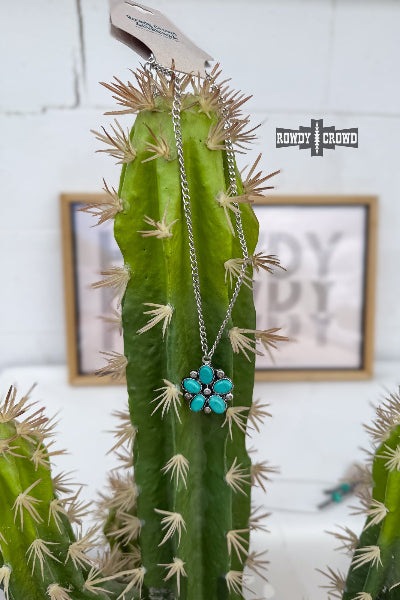 Necklace with a turquoise flower pendant hanging on a cactus plant.