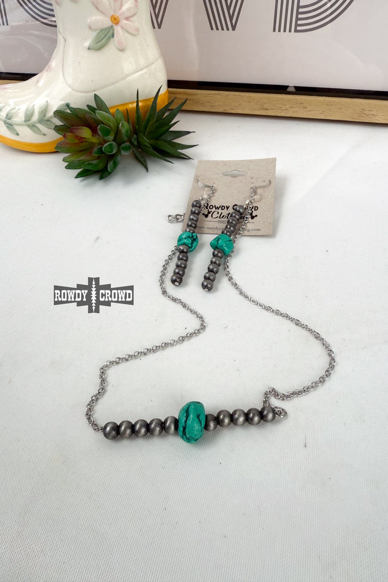 Necklace with turquoise beads on a white surface with a boot and plant in the background.
