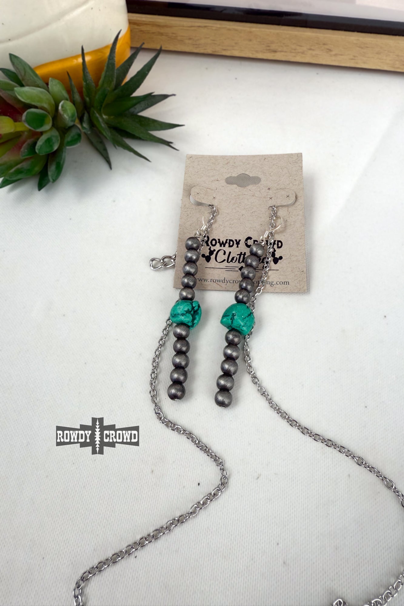 Necklace with beads and turquoise flowers on a white surface with 'Rowdy Crowd' branding.