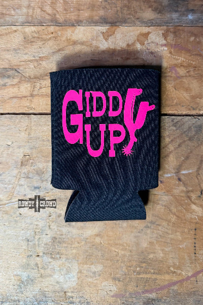 A black neoprene can cooler sleeve with a bright pink 'GIDDY UP!' graphic, displayed flat on a rustic wooden surface available at Cowtown Bling N Things.