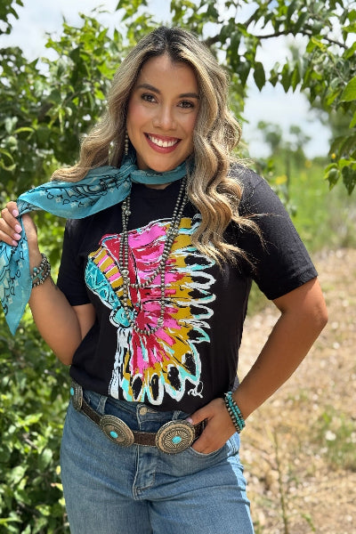 Woman wearing a colorful shirt with a scarf, standing outdoors with greenery in the background