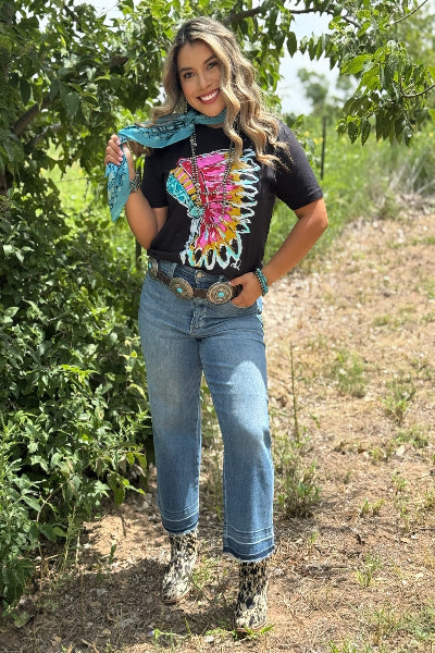 Woman standing outdoors with a colorful butterfly design on her shirt, surrounded by greenery.