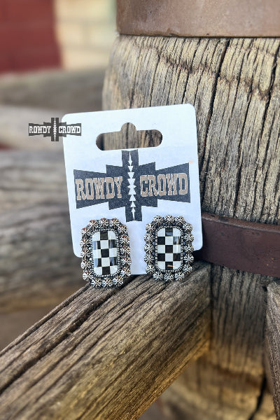 A pair of rectangular stud earrings with a black-and-white checkerboard center and silver-toned border, displayed on a white card labeled Rowdy Crowd. The card is resting on weathered wood available at Cowtown Bling N Things.