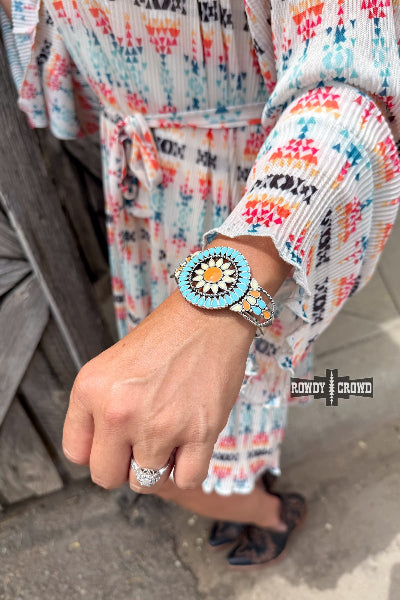 Person wearing a colorful dress with a turquoise and orange patterned watch on a blurred background