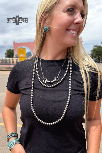 Woman wearing a black shirt with necklaces and earrings, standing outdoors.