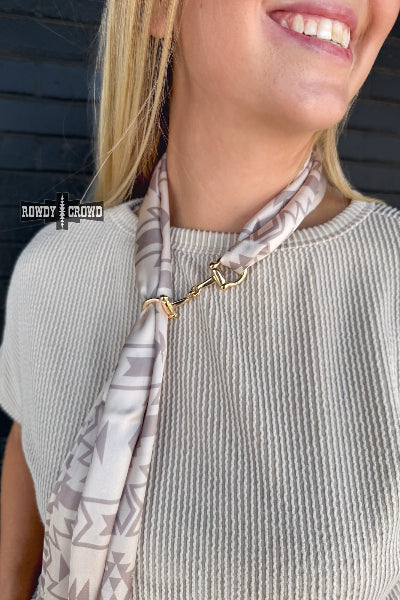 Woman wearing a patterned scarf with a gold clasp on a dark background