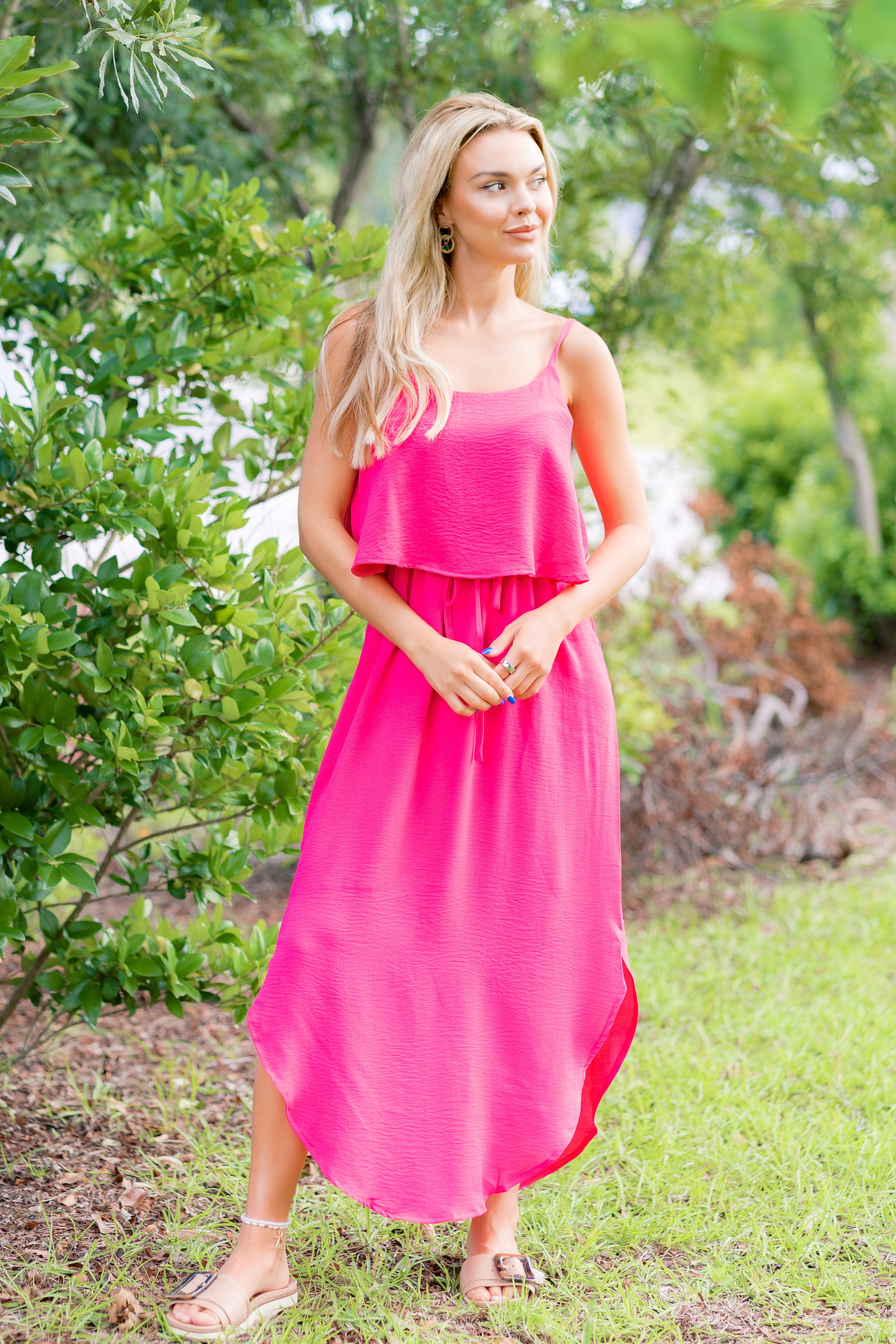 Woman in a pink dress standing outdoors with greenery in the background