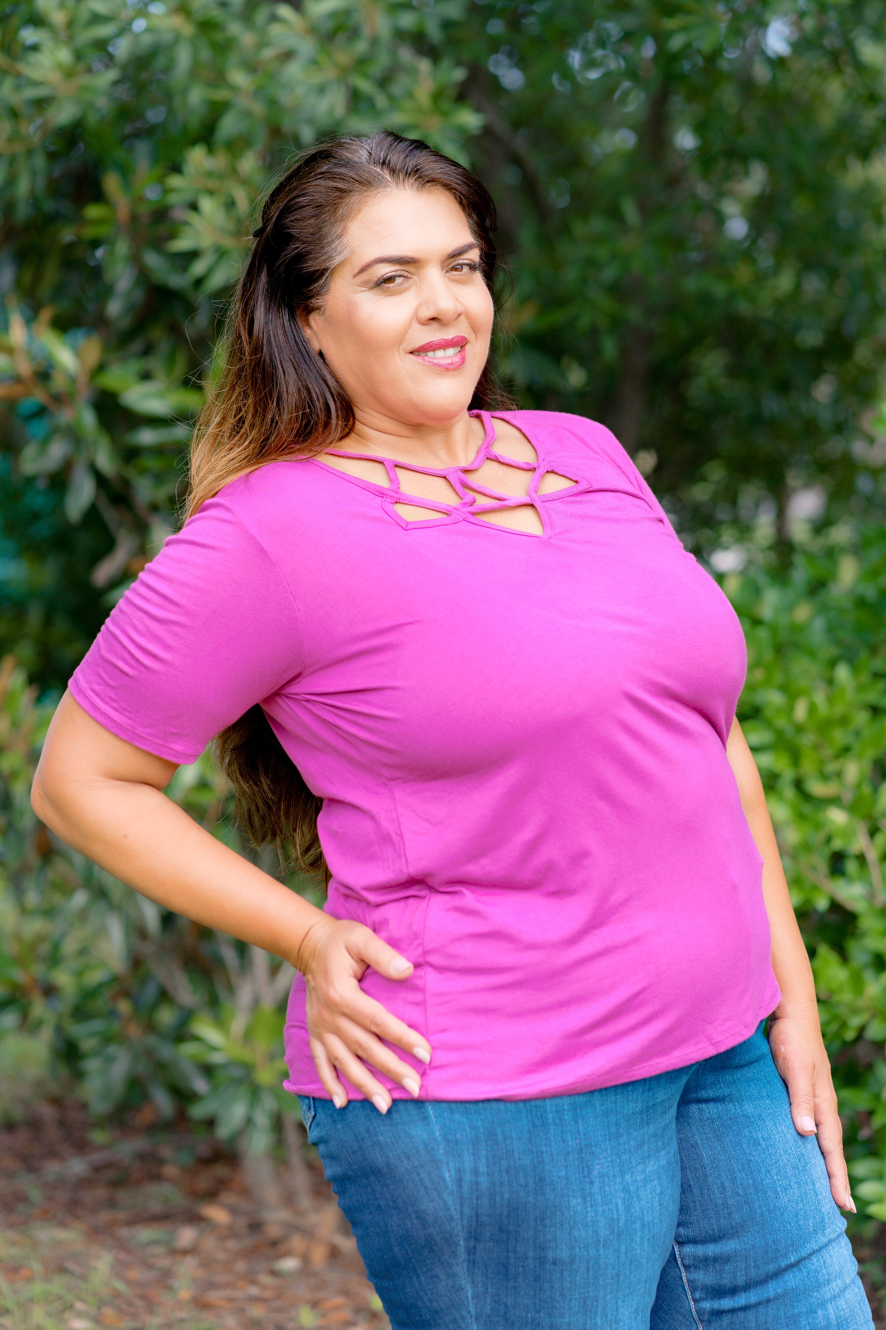 Woman wearing a pink top with cut-out design and blue jeans outdoors.