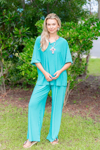 Woman wearing a turquoise outfit standing outdoors with greenery in the background
