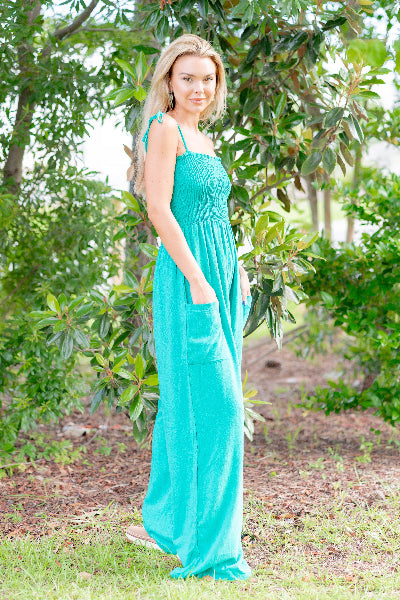 Woman in a teal dress standing in a natural setting with greenery.