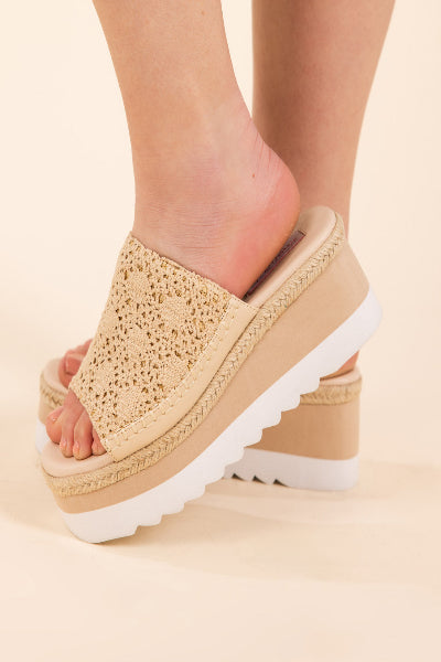 Beige open-toe sandals with white soles worn by a person on a beige background