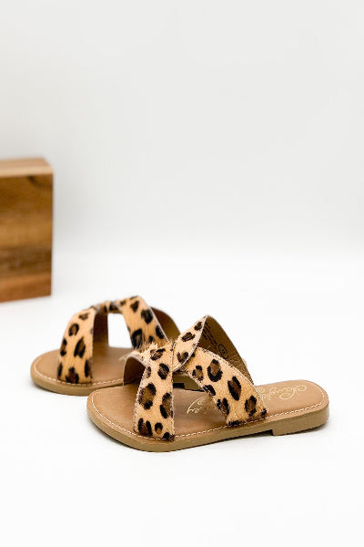 Leopard print sandals on a white surface with a wooden block in the background