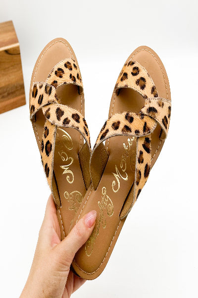 Pair of leopard print sandals held by a hand on a white background
