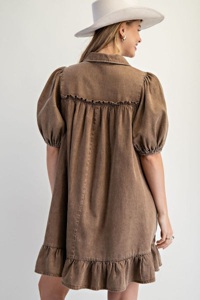 Woman wearing a brown dress with puffed sleeves and a white hat against a light background