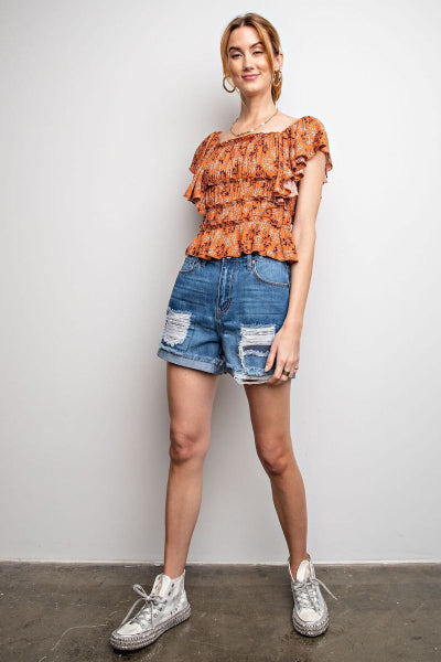 Woman wearing a patterned top and denim shorts against a plain background