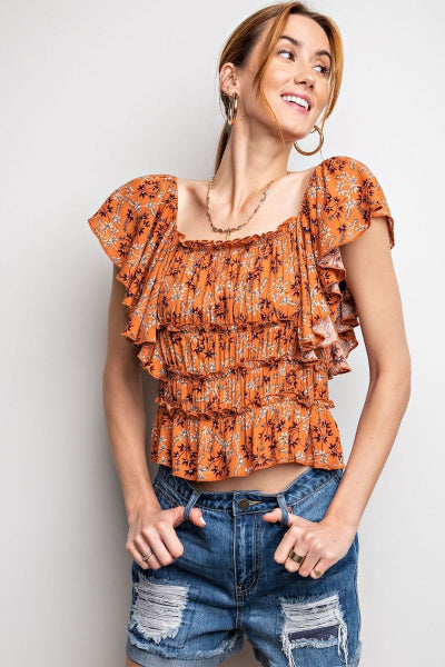 Woman wearing an orange floral top and blue jeans against a plain background