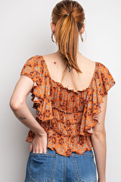 Woman wearing an orange floral top with ruffled layers against a plain background