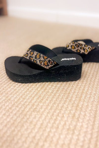 Black sandals with decorative straps on a textured surface