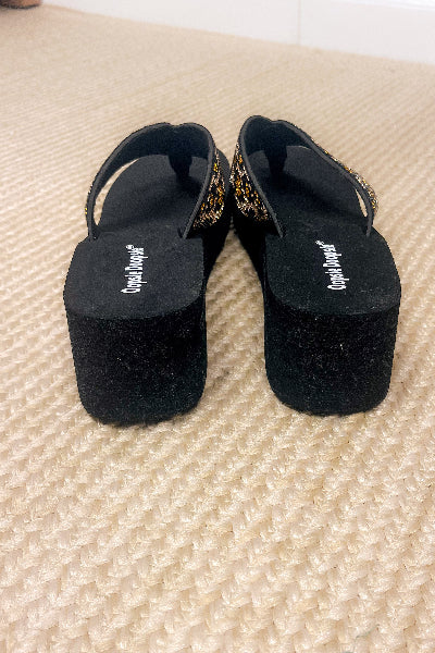 Black sandals with glittery straps on a textured beige surface