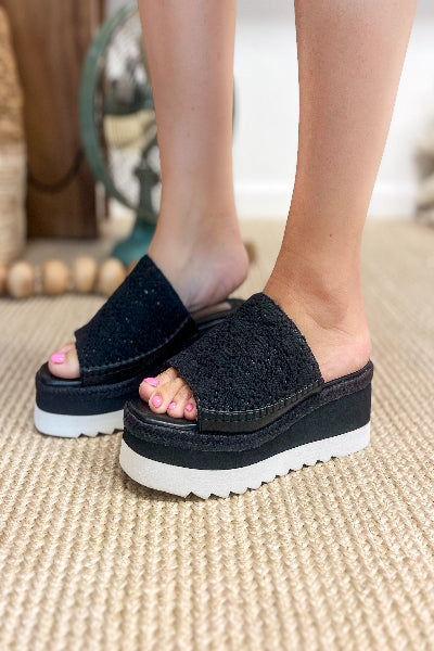 Black platform sandals worn by a person on a textured surface