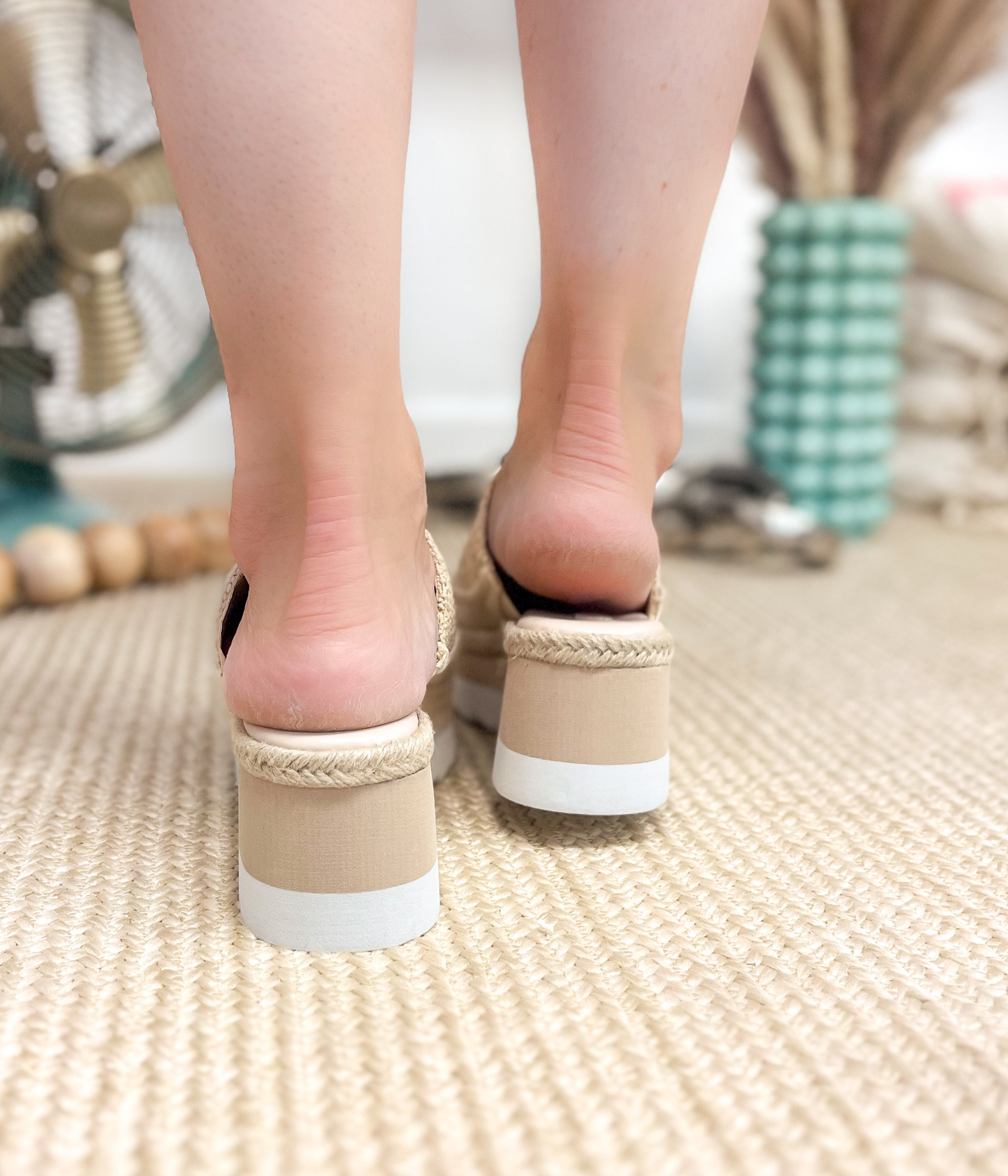 Close-up of feet wearing beige sandals with white soles on a textured floor.