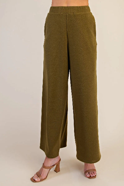 A person wearing olive green wide-leg cropped pants with a smocked waistband, paired with tan heeled sandals, shown against a plain beige studio background.
