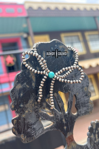 Necklace with turquoise bead on a decorative stand with 'Rowdy Crowd' branding, blurred background