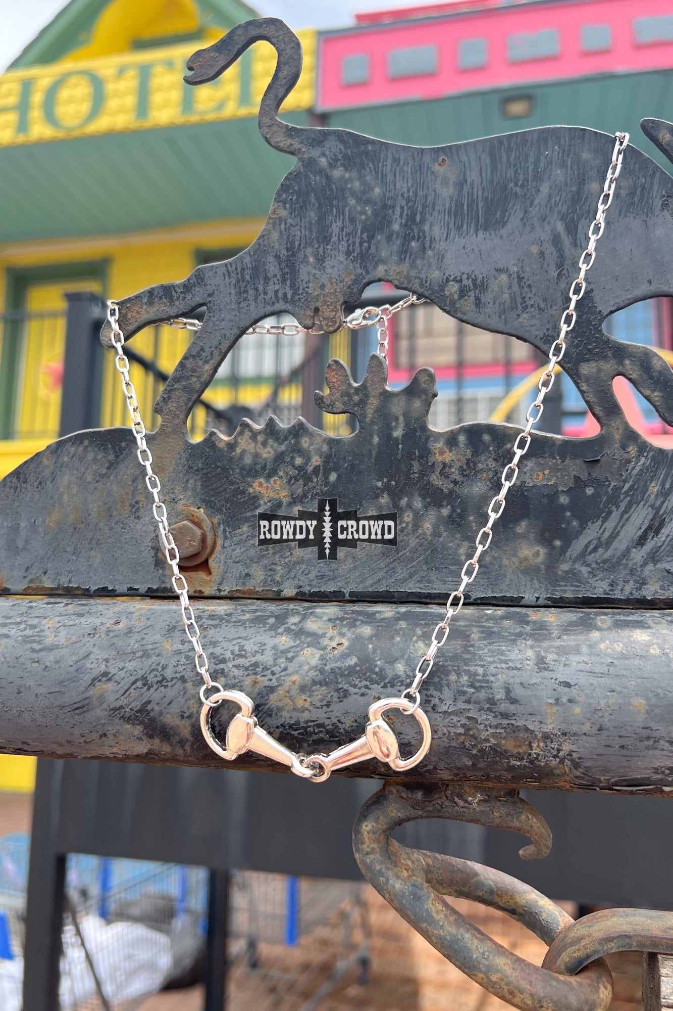 Silver bracelet with a horse bit charm on a metal surface with 'Rowdy & Rude' branding.