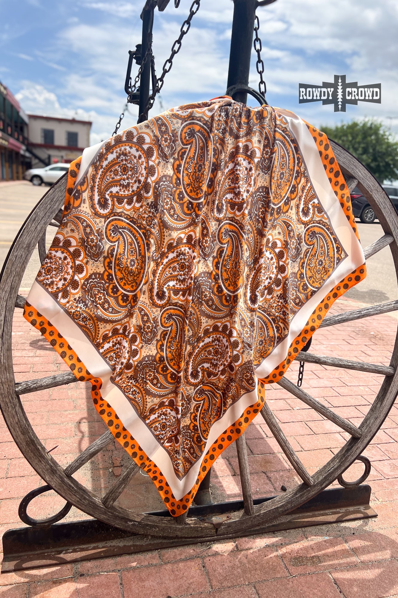 Paisley patterned blanket draped over a wooden wagon wheel with a building and sky in the background.