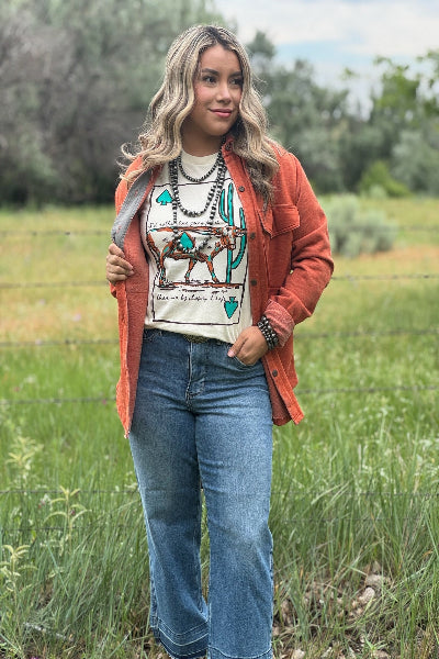 Woman wearing a graphic t-shirt, orange jacket, and blue jeans standing in a field.