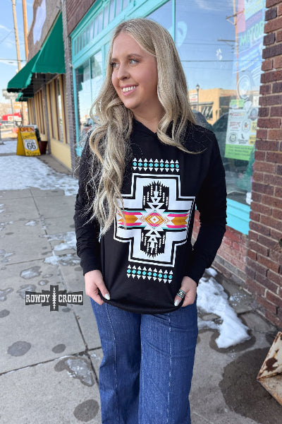 Woman wearing a black sweatshirt with a graphic design, standing on a sidewalk.