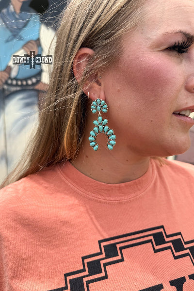 Person wearing turquoise earrings with a pink shirt featuring a geometric design.
