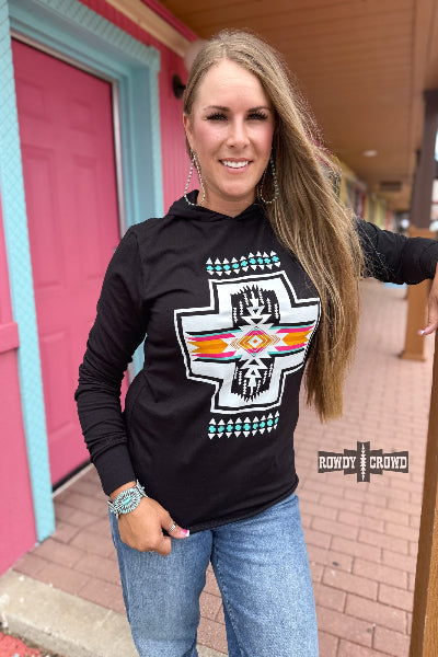 Woman wearing a black hoodie with a colorful design, standing in front of a pink building.