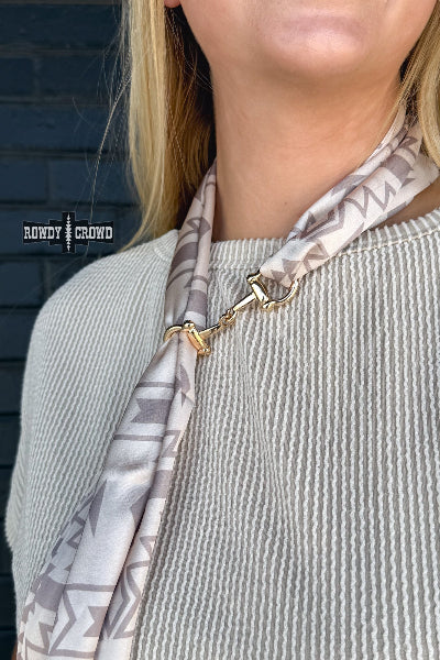 Person wearing a patterned scarf with a gold clasp against a dark brick wall.