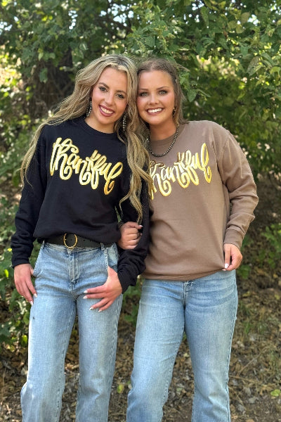Two women wearing 'thankful' sweatshirts standing outdoors with trees in the background available at Cowtown Bling N Things.