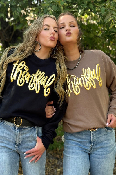 Two women wearing sweatshirts with 'thankful' printed on them, standing outdoors available at Cowtown Bling N Things.