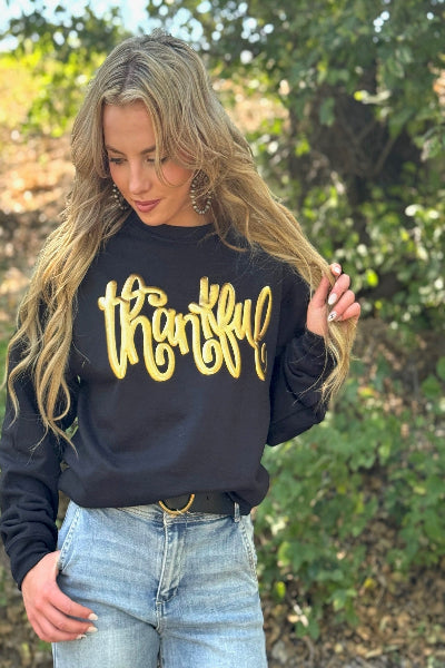 Woman wearing a black sweatshirt with 'thankful' in yellow text, standing outdoors available at Cowtown Bling N Things.