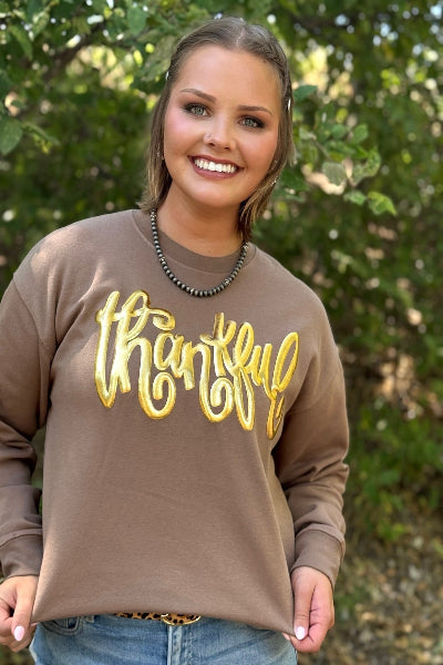 Woman wearing a brown sweatshirt with 'thankful' in gold letters, standing outdoors available at Cowtown Bling N Things.