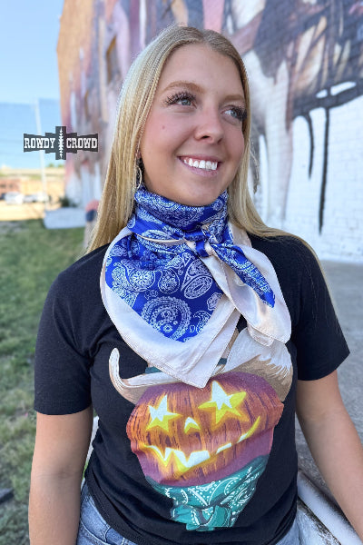 Bold blue paisley wild rag with cream trim styled for western wear, photographed folded on rustic wood