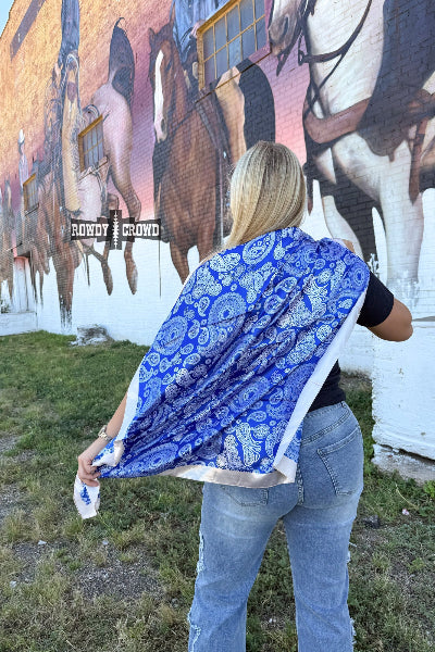 Bold blue paisley wild rag with cream trim styled for western wear, photographed folded on rustic wood