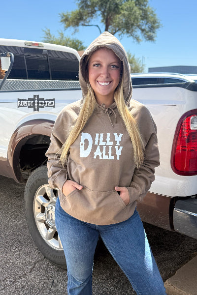 A woman wearing a brown hoodie with a white graphic that reads 'DILLY ALLEY' stands in front of a white pickup truck outdoors.