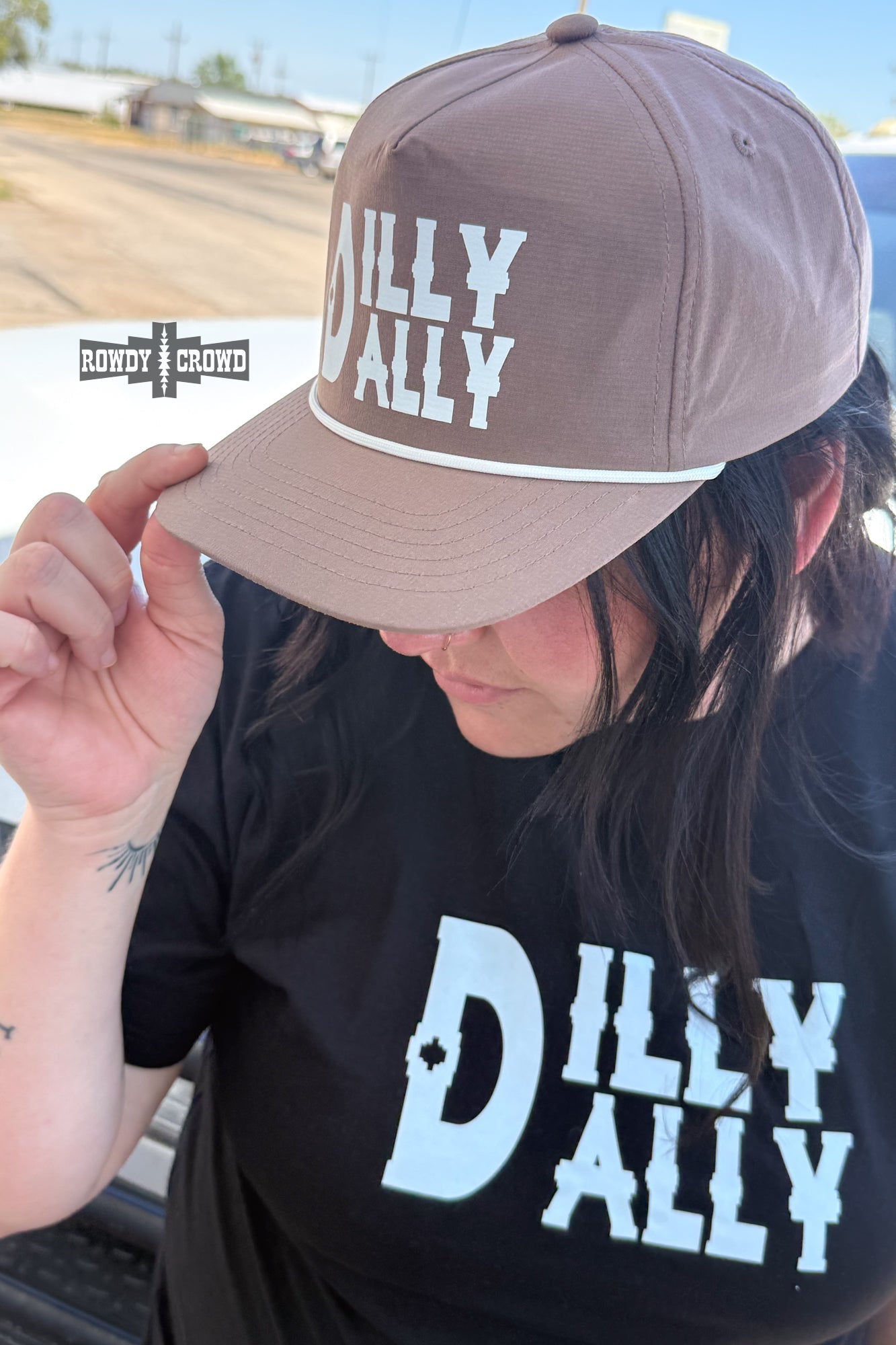 A person wearing a brown baseball cap with white 'DILLY DALLY' text and a matching black T-shirt, photographed outdoors near a vehicle. A 'HONOR CLOUD' watermark appears on the left.