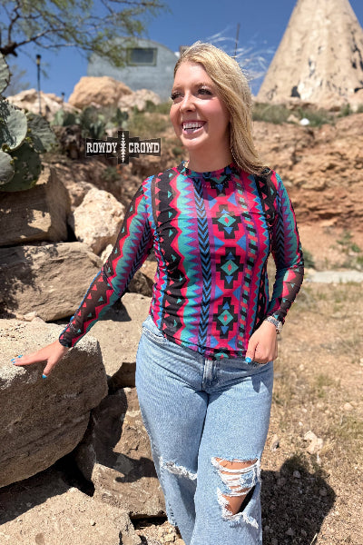 Woman wearing a colorful patterned shirt and jeans standing outdoors with rock formations in the background.
