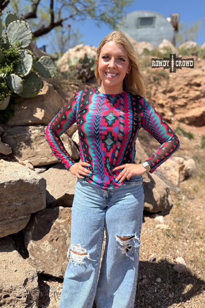Woman wearing a colorful patterned shirt and jeans standing in a desert landscape with cacti.