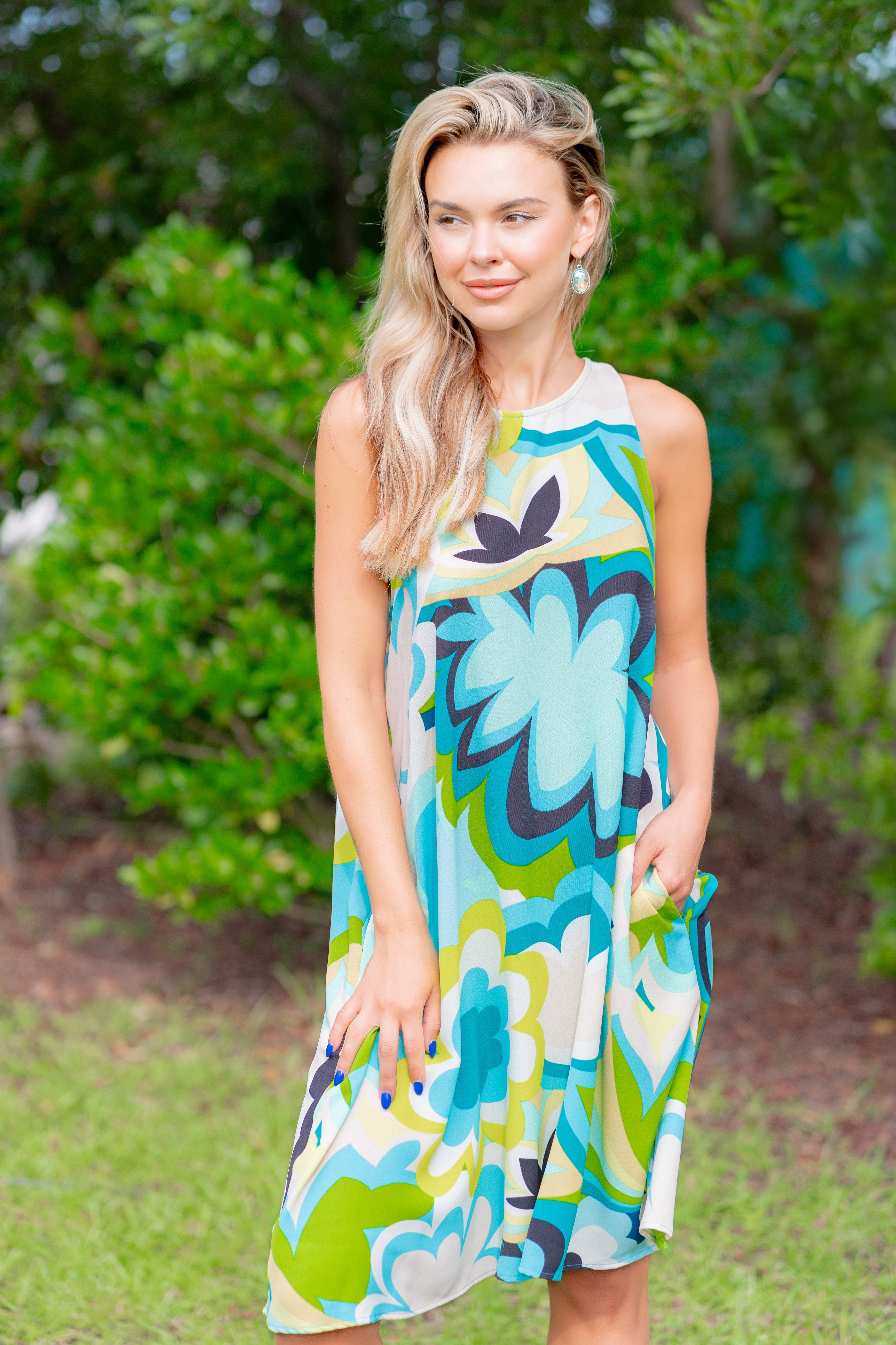 Woman wearing a colorful floral dress standing outdoors with greenery in the background