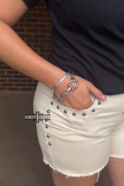 Person wearing a black shirt and beige shorts with visible jewelry, standing against a brick wall.