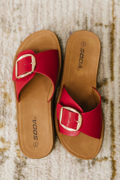 Red sandals with gold buckles on a textured surface