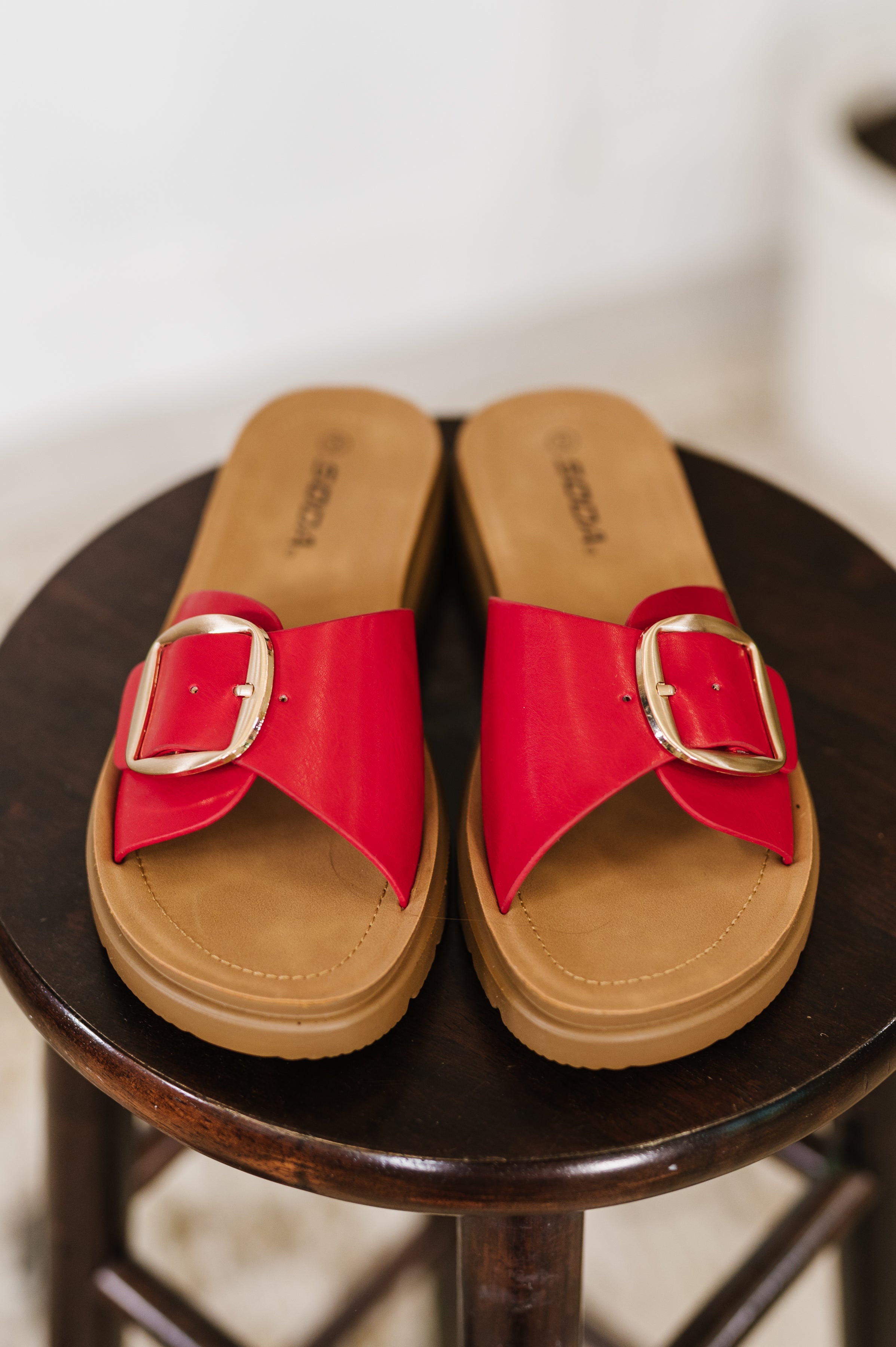 Red sandals with gold buckles on a black stool against a white background